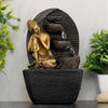 A water fountain featuring a golden statue of Buddha seated in meditation pose. Water flows from the Buddha's hands or from a nearby source, creating a serene and calming atmosphere. The fountain may be made of gold or a gold-plated material and may have additional decorative elements.